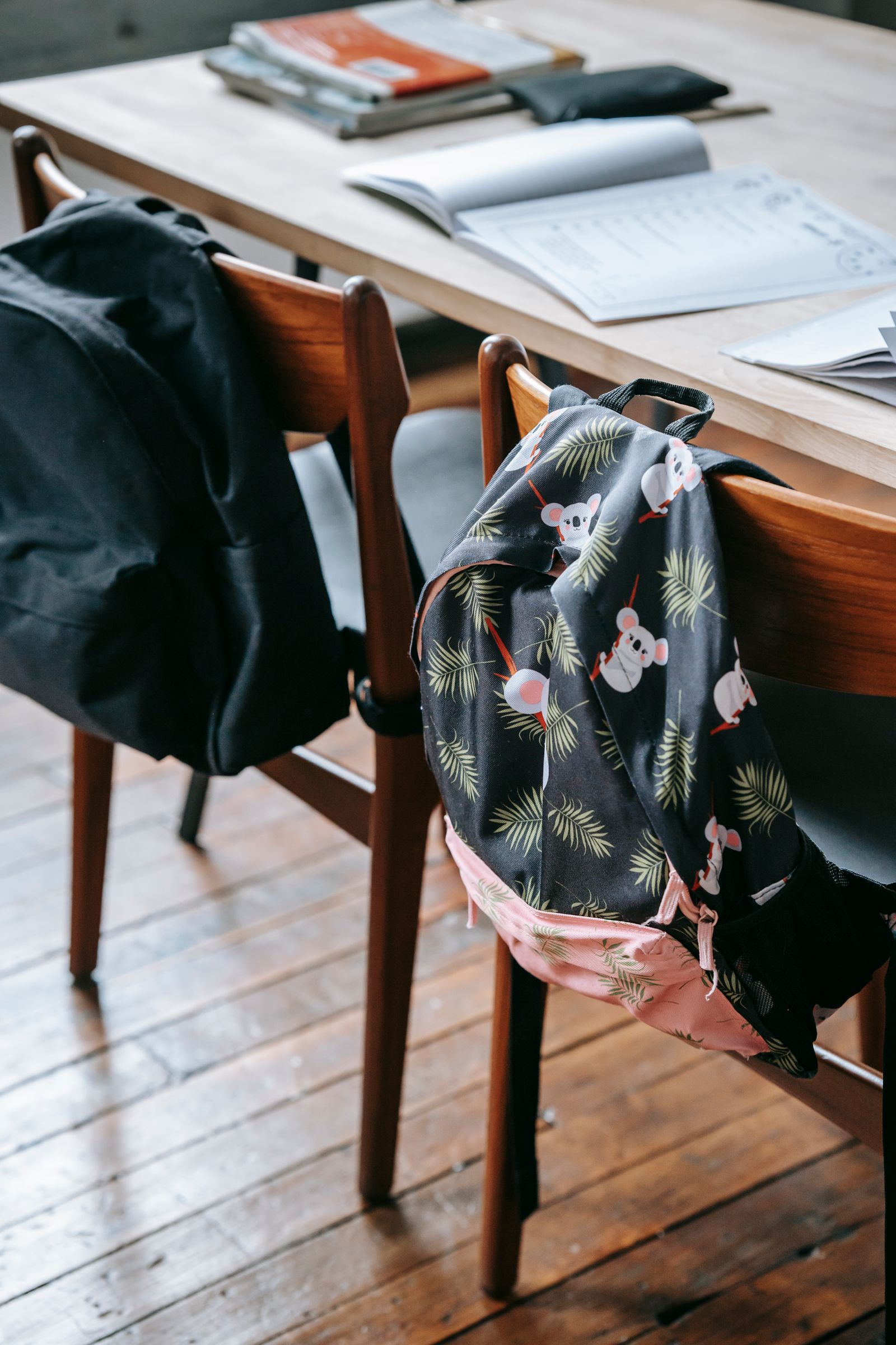 Two school backpacks hung on wooden chairs beside a table with an open notebook, ready for starting school gifts UK