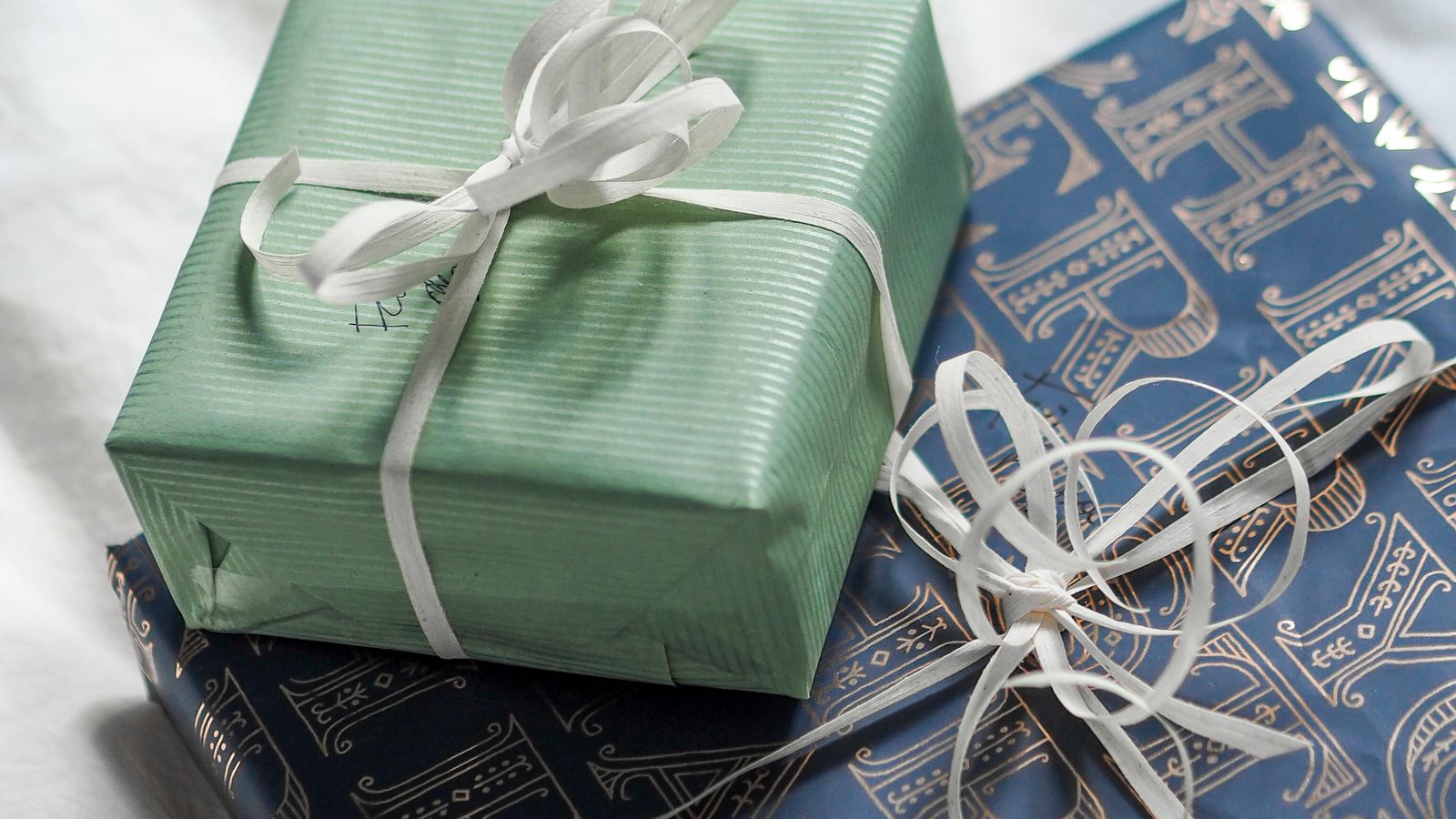 Two presents wrapped in sage green and navy paper tied with white ribbon, birthday gift for a friend's child UK