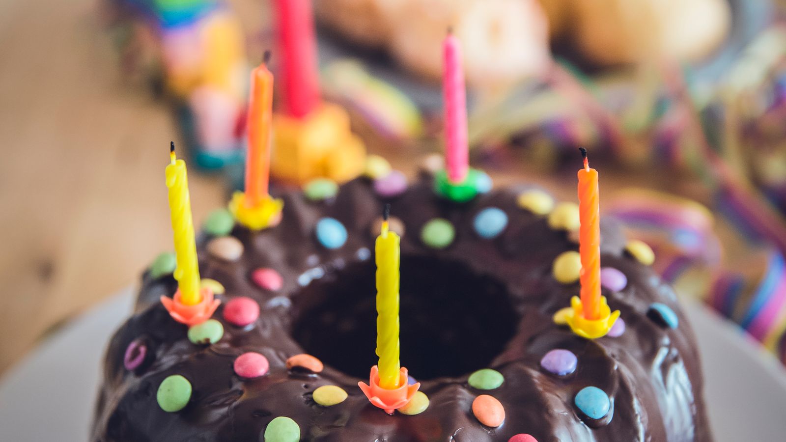 Chocolate birthday cake topped with lit candles and bright sweets, birthday gifts for 5 year olds UK
