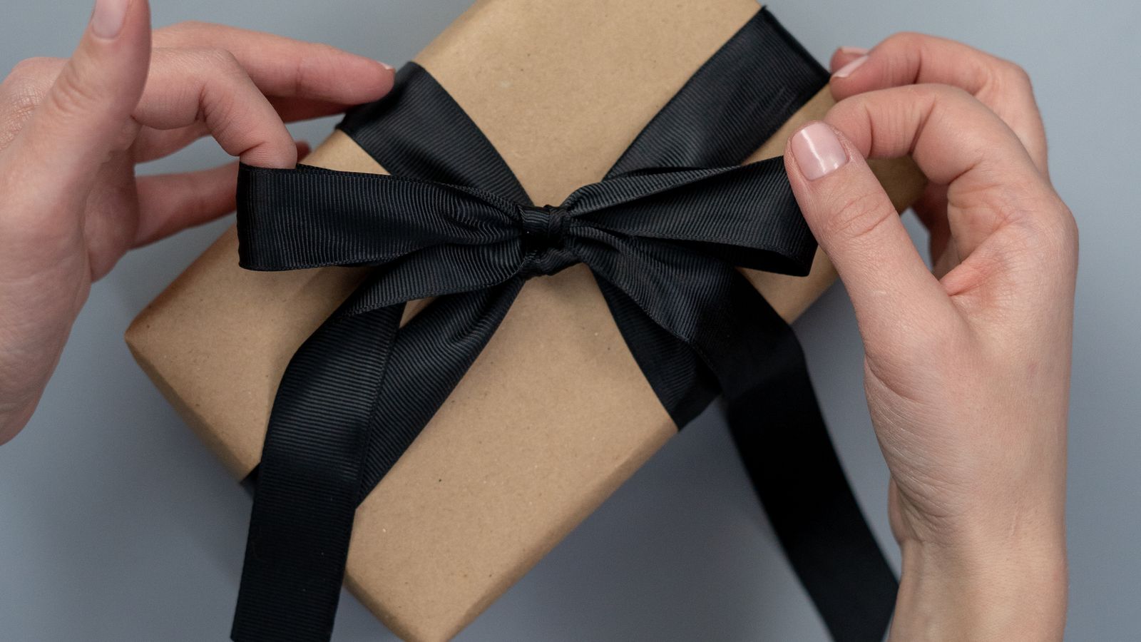 Hands tying a black ribbon around a present wrapped in brown kraft paper, birthday gifts under &pound;20 UK
