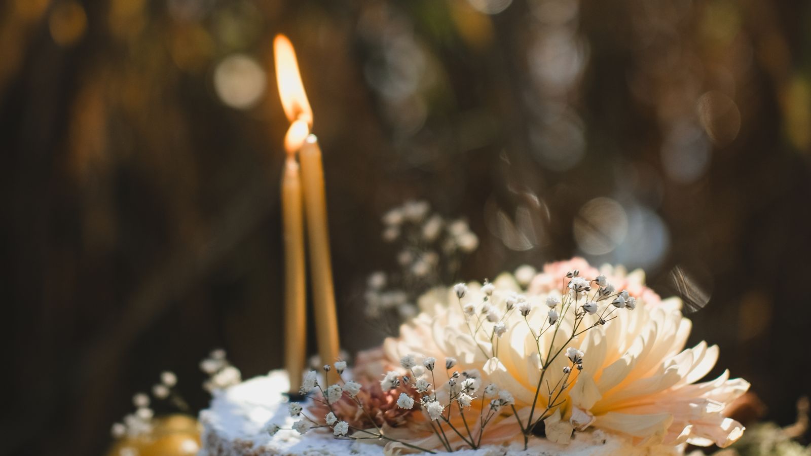 A single lit candle on a cream cake topped with flowers in warm evening light, first birthday gift ideas UK