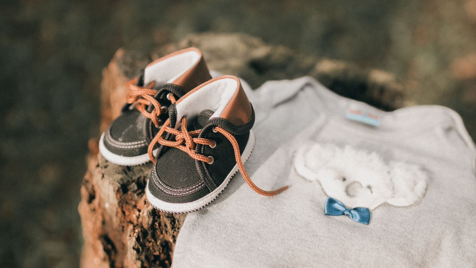 A pair of small baby shoes beside a grey bodysuit with a bear motif, new baby gifts UK
